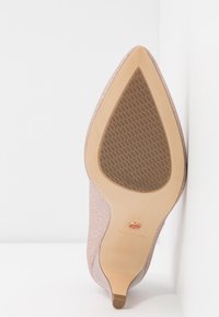 Chaussure à talon haut à paillettes roses à bout pointu montrant la semelle beige texturée et le talon étroit sur fond blanc.