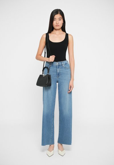 Bodysuit noir côtelé, jean en denim bleu taille haute à jambes larges avec ourlet effiloché, petit sac à main noir et escarpins blancs à bout pointu.