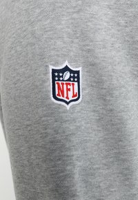 Tejido de sudadera gris con un parche del logo de la NFL en rojo y azul, en forma de escudo con un balón de fútbol y estrellas, bordado en blanco.
