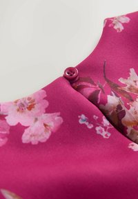 Tkanina w kwiatowy wzór w odcieniach różu z okrągłym dekoltem i ozdobnym fioletowym guzikiem na środku. Gładka tekstura.