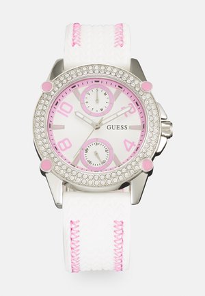 Srebrno-różowy zegarek na nadgarstek Guess z białą tarczą, pierścieniem wysadzanym kryształkami, dwoma małymi podtarczami wskazującymi datę i dzień oraz białym paskiem z różowym przeszyciem.