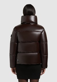 Brown glossy puffer jacket with a high collar, horizontal baffles, and a branded patch on the sleeve. Ribbed black skirt visible below.