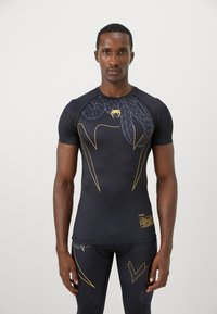 Sort sports T-shirt med korte ærmer, prydet med gule slange- og linjemønstre. Glat tekstur, tætsiddende design, fremtrædende logo på forsiden.