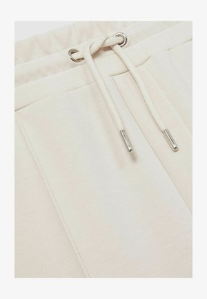 Bežinės sportinės kelnės su stringu, turinčios sidabrines akių detales ir minkštą tekstūrą, pasižyminčios lygaus audinio paviršiumi ir be raštų.