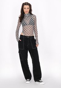 Fekete cargo nadrág fehér varrással, áttetsző, hosszú ujjú kockás bodysuit-al kombinálva. Az öltözet magas nyakú és oldalsó kivágásokat tartalmaz.