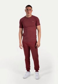 Bordeauxrotes Sportset bestehend aus einem kurzärmligen T-Shirt und Sweatpants. Glatter Stoff mit gerippten Bündchen und kleinem Logo auf dem Shirt.