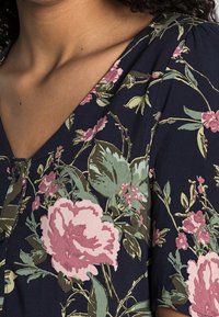 Abito con stampa floreale caratterizzato da uno sfondo blu scuro, peonie rosa pallido e fogliame verde, con scollatura a V e dettaglio di bottoni sul petto.