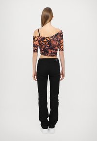 Kortermet, av-hodet crop topp i oransje og svart abstrakt mønster; kombinert med tettsittende svarte jeans og hvite sko.