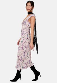 Blumiges Midikleid in zartem Rosa mit lila und grünen Akzenten, mit kurzen Ärmelchen, figurbetontem Schnitt und gerafftem Saum. Kombiniert mit schwarzen Wildlederstiefeln.