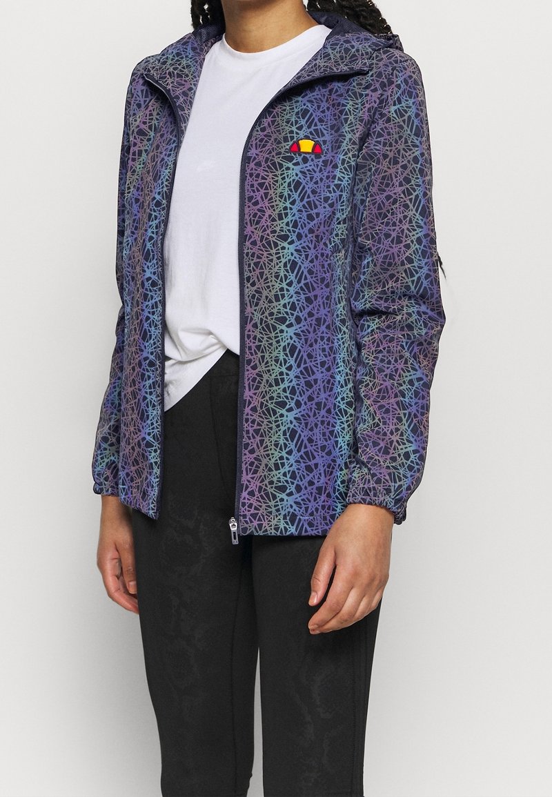 Lätt zip-up jacka med ett flerfärgat geometriskt mönster i lila, blått och grönt. Har en liten broderad logotyp på bröstet.