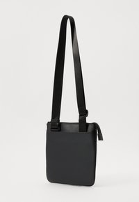 Crna torba za crossbody nošenje s teksturiranim vanjskim dijelom, podesivim remenom, dva gornja zatvarača i uskim pravokutnim oblikom. Mekan, lagan materijal.