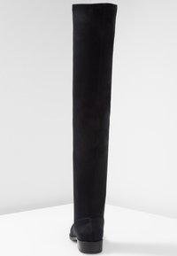 Botas negras por encima de la rodilla hechas de material sintético suave, con un diseño ajustado y un tacón bajo apilado. Presentan detalles de costura visibles.