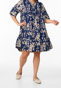 Robe fleurie bleu marine à manches courtes, décolleté en V et jupe à volants ; présente des motifs de feuilles couleur crème et des détails de couture texturés.