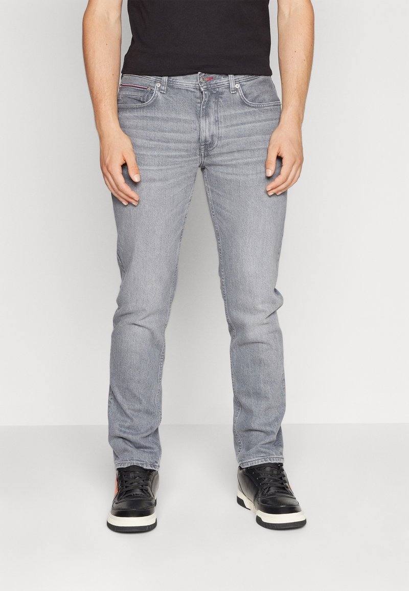 Vaqueros de mezclilla gris claro con un ajuste ajustado, con sutiles desgastes, diseño clásico de cinco bolsillos y zapatillas negras de caña alta.