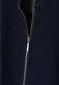 Nära bild av en delvis öppnad silverfärgad metallblixtlås på mörkblå denimtyg.