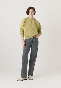 Olívazöld kapucnis pulóver elülső zsebbel és állítható kapucnival, magas derékú, egyenes szárú szürke farmernadrággal és törtfehér loafers cipővel párosítva.