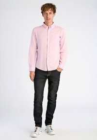 Lichtroze overhemd met lange mouwen en knopen, met kraag en zak, gecombineerd met donkere jeans en witte sneakers met gekleurde accenten.