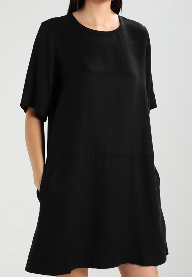 Robe noire à manches courtes en tissu lisse, avec un col rond, une coupe ample et des poches latérales. Design simple et minimaliste.