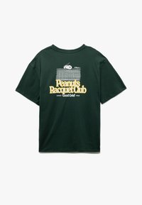 Czarna zielona koszulka z krótkim rękawem z motywem Snoopy'ego wyglądającego zza siatki tenisowej oraz żółtym napisem "Klub Rakietowy Peanuts od Good Grief 1950" z tyłu.