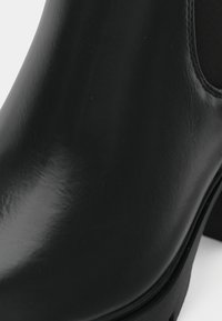 Svart läderstövel till ankeln med glansig yta, rundad tå, elastiska sidopaneler och en kraftig sula. Mjuk textur med minimal detaljering.