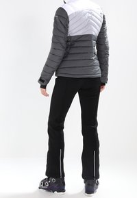 Grå och vit puffjacka med chevrondesign, i kombination med svarta byxor. Egenskaper inkluderar dragkedjor vid anklarna och skidstövlar med spännen.