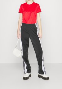 Červené texturované tričko, černé sportovní kalhoty s bílými bočními pruhy, doplněné bílou kabelkou a chunky botami na černé podrážce.