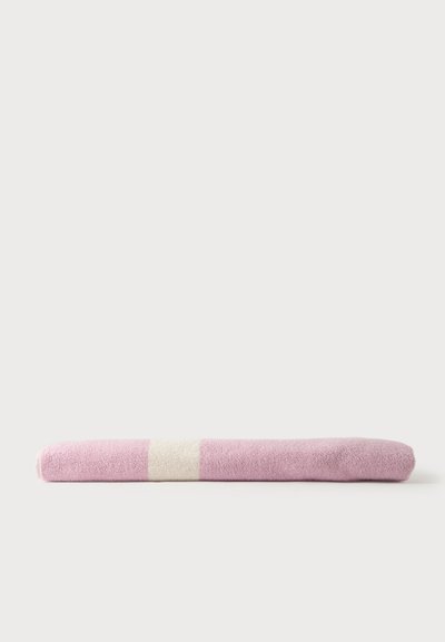 Serviette rose roulée avec une bande blanche au centre, placée horizontalement sur une surface blanche.