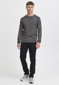 Pull gris à manches longues avec un design texturé, un col rond et des poignets côtelés, associé à un jean noir et des baskets grises.