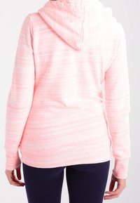 Sudadera de color rosa claro con un diseño texturizado y a rayas, que cuenta con capucha y puños de canalé, llevada sobre pantalones oscuros.
