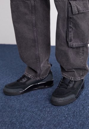 Schwarze Sneaker aus einer Mischung aus Veloursleder und strukturiertem Stoff mit flacher Sohle und dezenten Akzenten. Kombiniert mit lockeren grauen Cargohosen.