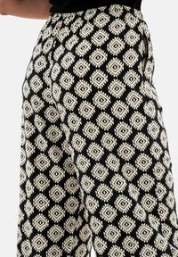 Pantalones de patrón en blanco y negro que presentan un diseño geométrico de diamantes con acentos marcados y una cintura fruncida para un ajuste ajustable.