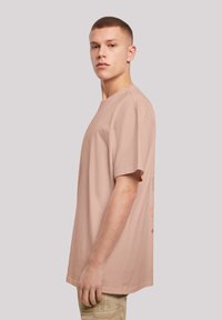 Světle růžové bavlněné tričko s volným střihem, krátkými rukávy a kulatým výstřihem. Na zádech má grafický potisk.