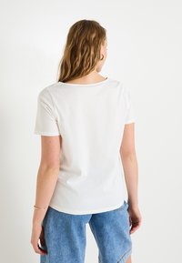 Camiseta blanca de manga corta con cuello redondo. Material de algodón suave y corte relajado, combinada con pantalones cortos de denim azul. Diseño minimalista.