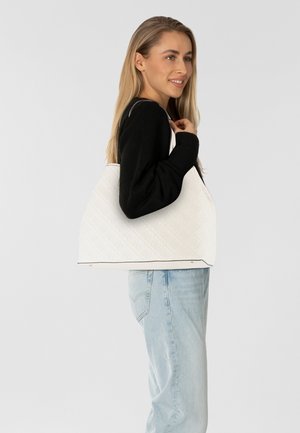 Witte handtas met een gewatteerde textuur en subtiel patroon. Heeft een gestructureerde vorm en zwarte details, gedragen door iemand in casual kleding.