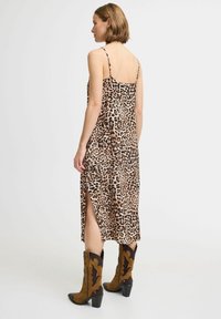 Abito midi a stampa leopardata con spalline sottili, spacco laterale e una texture di tessuto liscia. Indossato con stivali alla caviglia in stile western marroni e neri.