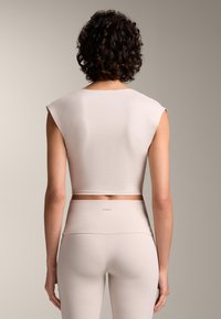 Svijetlosmeđi top kratkih rukava, glatke teksture i okruglog dekoltea, u kombinaciji s odgovarajućim hlačama visokog struka.