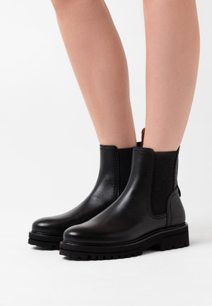Botas Chelsea de cuero negro con paneles laterales elásticos, suelas de goma robustas y una lengüeta para ponérselas fácilmente. Textura suave y diseño elegante.