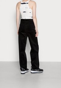 Zwarte corduroy wijde broek met een hoge taille, gecombineerd met een witte tanktop met een tie-dye patroon. Zwarte sportschoenen.