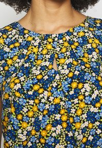 Abito floreale a maniche corte con sfondo nero, caratterizzato da fiori gialli e blu sparsi, scollatura rotonda e dettaglio a chiave plissettato.