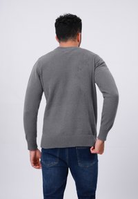 Gray knitted sweater with long sleeves, a round neckline, and ribbed cuffs and hem. Paired with dark blue denim jeans.
