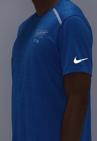 Blauwe Nike T-shirt met een gestructureerd patroon, featuring een witte logo op de borst en een witte accent op de schouder. Korte mouwen.