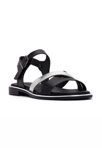 Sandali in pelle nera con cinturino argentato, design incrociato, fibbia regolabile, suola piatta e sottile bordo bianco.