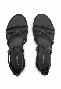 Sandales noires avec plusieurs sangles croisées, semelles plates et fermeture éclair au talon. Fabriquées en matériau lisse, avec un logo de marque discret.