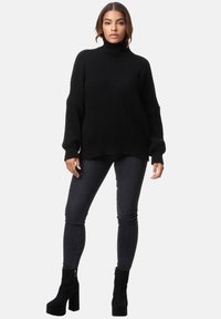 Schwarzer gerippter Rollkragenpullover mit langen Ärmeln, oversized Fit. Kombiniert mit dunklen Skinny-Jeans und schwarzen Plateau-Stiefeletten.