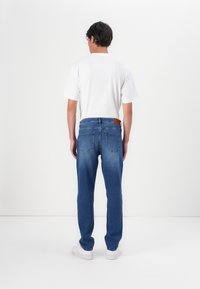 Jeans de denim ajustados en un lavado azul medio con una textura suave, cinco bolsillos y un parche de cuero marrón en la cinturilla trasera.