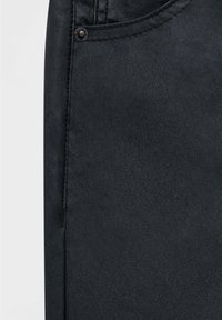 Telaje de mezclilla negra que muestra una textura detallada con un bolsillo visible y un acento de remache metálico. El material parece suave con un ligero brillo.