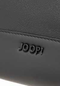 Borsa a mano in pelle nera con esterno testurizzato, accenti lisci e logo impresso. Dettagli includono cuciture fini e un design elegante.