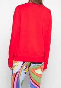 Sudadera roja de manga larga, con puños y dobladillo acanalados, hecha de material suave. Combinada con leggings coloridos y con estampado.