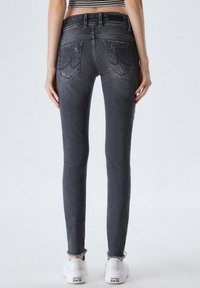 Jeans ajustados grises con una cintura alta, que presentan detalles desgastados y un dobladillo deshilachado. Combinados con zapatillas blancas. Vista trasera.