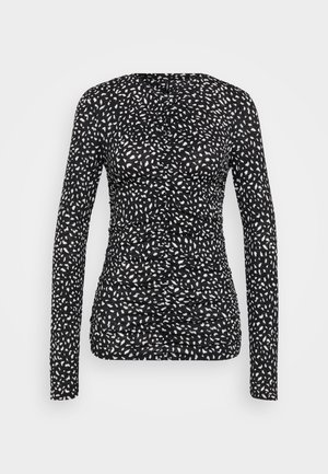 Top à manches longues en noir avec un motif de points irréguliers blancs. Présente un design froncé avec un tissu texturé, une silhouette ajustée et un col rond.